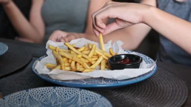 Bir çocuk, kıtır kıtır, altın patates kızartmasını sosa batırmak için can atıyor. Yakın çekim, bu basit çocukluk ikramından zevk almanın saf zevkini yakalar..