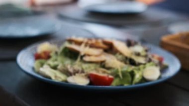 Cazip bir Sezar salatası, biraz bulanık, bir restoranda mavi bir tabakta duruyor. Bulanık efekt, lezzetli yemeğin geleceğini seziyor..