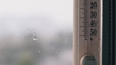Yağmurlu bir pencereye monte edilmiş bir termometre, serin ve ıslak havayı gösteren 10 santigrat derece sıcaklığı gösterir..