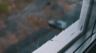 Arka planda bulanık şehir manzarası olan bir pencereye yağan yağmurun yavaş çekim görüntüleri. Sahne, şehir ortamında yağmurlu bir günün güzelliğini ve huzurunu yakalıyor..
