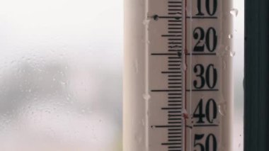 Yağmurla kaplı bir pencereye bağlı bir termometre, serin ve nemli hava koşullarını vurgulayan 10 derece Celsius sıcaklığı gösterir..