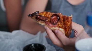 Bir çocuğun sosisli pizza diliminden bir ısırık alıp sağlıksız yemek seçimlerini ve çocukluk obezitesini vurguladığı yakın çekim..