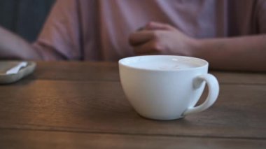 Bir bardak kapuçino ve latte sanatı sizi bir yudum içmeye ve anın tadını çıkarmaya davet eden ahşap bir masada otururlar..