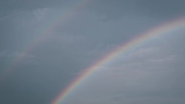 Büyüleyici çift gökkuşağı bulutlu gökyüzünü süslüyor. Yağmurdan sonraki umut ve güzelliğin sembolü. Bu büyüleyici sahne huzuru ve merakı uyandırıyor..