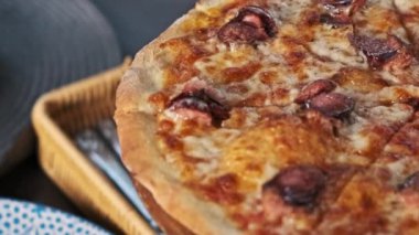 Sosisli ve erimiş peynirli taze bir pizza, dilimlenmiş ve bir restoran masasında eğlenmeye hazır..