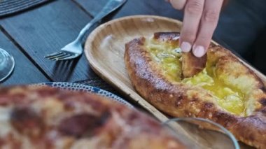 Adjarian Khachapuri 'nin peynirli bir parçasını çeken bir kadının yakın plan fotoğrafı. Yumurta sarısı olan geleneksel bir Gürcü yemeği..