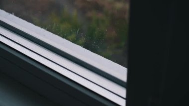 Arka planda bulanık bir kırsal manzarayla pencereye yağan yağmurun sakin, yavaş çekim görüntüleri. Sahne, yağmurlu bir günün güzelliğini ve huzurunu yakalar..