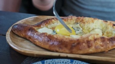 Geleneksel bir Gürcü yemeği olan ucuz bir Adjarian khachapuri ile yumurta sarısını karıştırıp zengin lezzet ve dokuları ön plana çıkaran bir kişi..