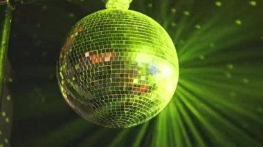 Parlak bir disko topu sallanır ve yavaşça döner, yeşil ve mavi lazer ışınlarıyla aydınlatılarak, bir parti veya gece kulübü sahnesi için büyüleyici bir görsel efekt yaratır..