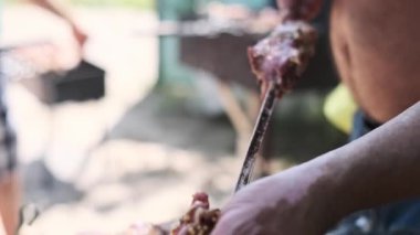 Bir adam ustalıkla terbiye edilmiş et parçalarını şişe geçirir ve onları ızgaraya hazırlar. Bu yakın çekim lezzetli şiş kebap yapma sürecini yakalar..