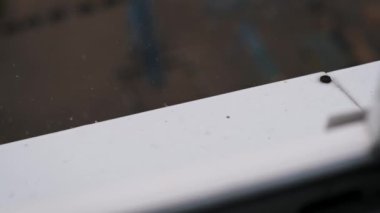 Pencerenin kenarından düşen yağmur damlalarının yakın çekim görüntüsü bulanık arka planda büyüleyici bir su damlası dansı yaratıyor..