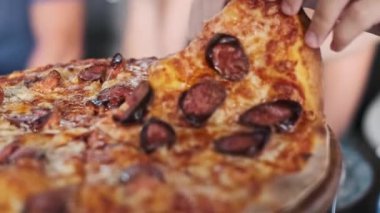 Yakın plan çekimde bir dilim pizzayı sosisle yakalar, yemeği paylaşmayı ve birlikte yemek yemeyi önemserler..