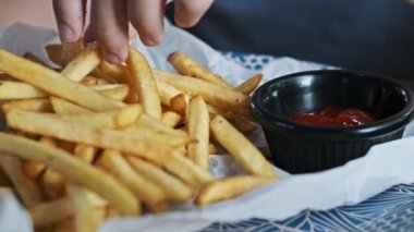 Bir çocuğun, altın bir patates kızartmasını ketçapa batırıp klasik bir zevke daldırdığı yakın plan görüntüsü..