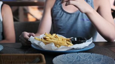 Çocuk bir tabak kızarmış patatese doyuyor ve her birini bir kafede ketçapa batırıyor. Gündelik yemek atmosferi ve çocuklar yiyeceğe odaklanıyor. Çocukluktan gelen keyifli bir ortam yaratıyorlar.