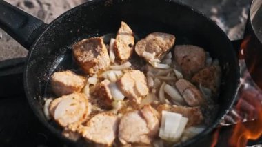 Tavuk ve soğan parçaları bir kamp ateşinin üzerinde cızırdıyor, havayı lezzetli bir aromayla dolduruyor. Kırsal bir açık hava yemek sahnesi..