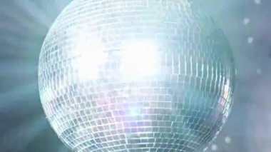 Bir disko topu parlak spot ışıkları altında asılı durur ve döner, etrafındaki uzaya renkli yansımalar yapar. Karanlık arka plan, tipik gece kulübü atmosferi. Eğlence, parti, müzikle ilgili görseller