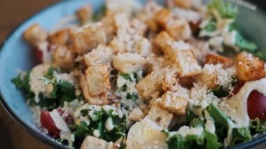 Bir Sezar salatasının yakın plan çekimi çıtır kıtır kıtırları, rendelenmiş parmesan peynirini, taze marulu ve sulu domatesleri ön plana çıkararak ağız sulandıran görsel bir deneyim yaratıyor..