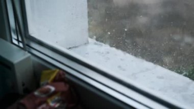 Camdan süzülen yağmurun büyüleyici bir su damlası görüntüsü oluşturduğu pencerenin yakın plan görüntüsü. Bulanık dış görünüş dışarıda fırtınalı bir günde.