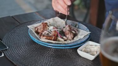 Bir adam, yanında bir bardak bira ve sosla birlikte pide ve soğanlı bir tabaktan ızgara et toplamak için çatal kullanıyor..