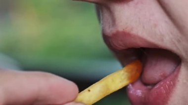 Yakın çekimde, bir çocuğun ağzının patates kızartması yerken ki görüntüsü, yan görüş. Sağlıksız yeme alışkanlıkları, abur cubur, çocukluk obezite konsepti.