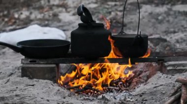 Kamp ateşi, dökme demir çaydanlığı, tencereyi ve kızartma tavasını ısıtarak, kırsal alanda yemek pişirme ve vahşi yaşam macerası sahnesi yaratıyor..