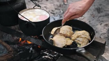 Sulu tavuk butları kamp ateşinin üstünde tavada kızartılır. Kırsal kamp sahnesi macera ve açık hava yemeklerini çağrıştırıyor..