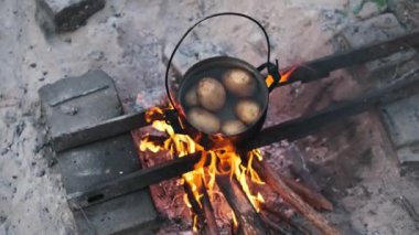 Açık bir kamp ateşinin üzerinde patates kaynayan taşralı yemek sahnesi, açık hava macerası hissi uyandırıyor..