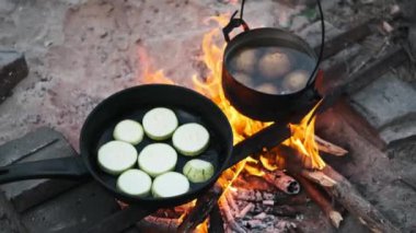 Bir tencere patates haşlanıyor ve kabak bir kamp ateşinin üzerinde cızırdıyor, kırsal ve lezzetli bir açık hava yemeği yaratıyor..
