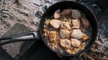 Kamp ateşinde tavada kızaran tavuk ve soğan yakın çekim. Tavuk kahverengileri ve cızırtıları lezzetli bir aroma yaratıyor..