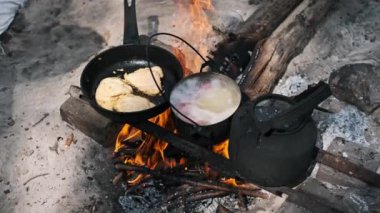 Kamp ateşi, tavada tavuk pişirirken ve bir tencere çorba içerken ışıl ışıl yanar. Kurumuş bir çaydanlık ateşte oturur, çaya hazır..