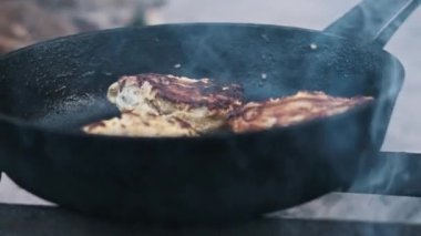 Üç tavuk budu bir kamp ateşinin üstünde kızarır ve kırsal alanda pişirmenin cazibesini yakalar..