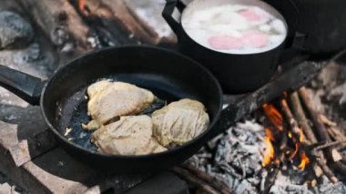 Tavada cızırdayan tavuk ve kamp ateşinde kaynayan çorba ile kırsal açık hava yemek sahnesi..