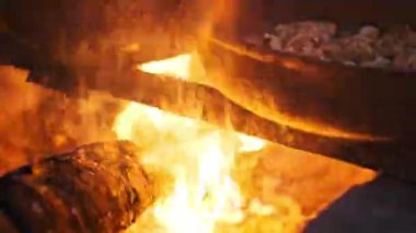 Yoğun turuncu alevler, yemek pişirmek için kullanılan bir kamp ateşinde odun yakar. Büyüleyici bir ısı ve ışık gösterisi yaratır..