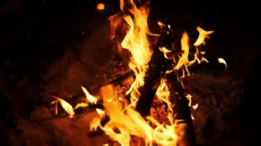 Karanlığı aydınlatan parlak turuncu alevlerle yanan bir kamp ateşine yakın çekim yapmak sıcak ve samimi bir atmosfer yaratır..