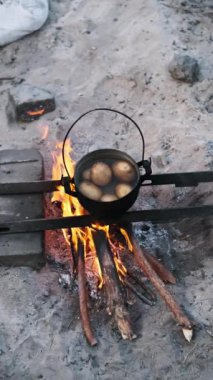 Kumsalda kamp ateşinin üzerinde patates kaynıyor. Doğal ateş ile kırsal açık hava yemekleri. Kamp, hayatta kalma, basit hayat kavramları..