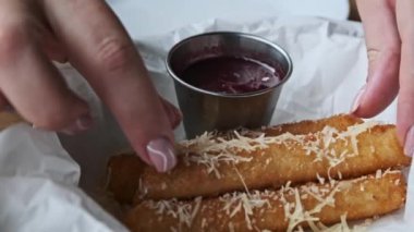Kadınların ellerinin, lezzetli kızarmış peynirli çubukları parmesanlı yaban mersini sosuna batırıp restoran atmosferini gösteren yakın plan görüntüsü..