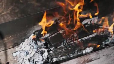 Sıcak turuncu alevlerle yanan kamp ateşi ve parlak közler, açık hava barbeküsü için sıcaklık ve ortam yaratıyor..