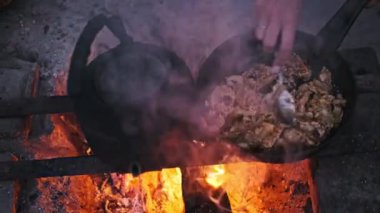 Bir adam kamp ateşinin üstünde et pişirirken yakınlarda bir çaydanlık oturuyor. Açık hava yemekleri, kırsal yaşam tarzı konsepti..