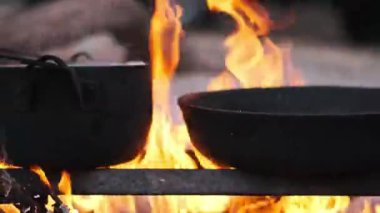 Kamp ateşi, siyah bir tencere ve metal ızgarada dinlenen bir tavayla ışıl ışıl parlar. Sağlıklı bir açık hava yemeği için mükemmeldir..