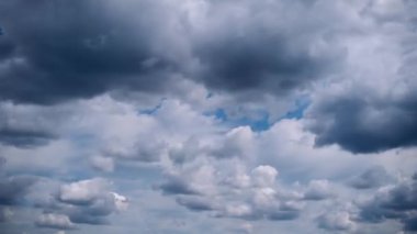 Koyu, kasvetli yağmur bulutları, tüylü, beyaz kümülüs bulutlarıyla karışmış, parlak gök yüzünde hızla hareket ederek büyüleyici bir atmosferik ekran yaratıyor..