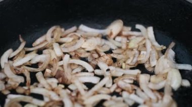 Bir tavada kızaran dilimlenmiş soğanların yakın plan çekimi, pişerken dokularını ve altın-kahverengi renklerini gözler önüne seriyor..