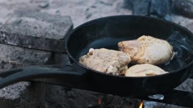 Üç baharatlı tavuk budu bir kamp ateşinin üstünde cızırdıyor, açık hava pişirme sanatını sergiliyor..