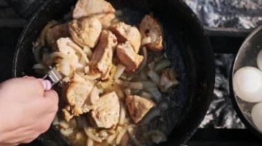 Tavuk ve soğan cızırdıyor ve kamp ateşinin üzerinde bir tavada pişiriyor, dışarıda nefis bir yemek sahnesi yaratıyor. Altın sarısı et ve karamelli soğan lezzetli ve basit bir kamp ateşi yemeği vadediyor..
