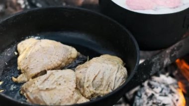Kamp ateşinde tavada et kızartmak, açık hava yemeklerinin klasik bir görüntüsü..