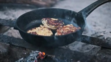 Cızırdayan tavuk biftekli dökme demir bir tava kamp ateşinin üzerine konur ve dışarıda lezzetli bir yemek pişirilir..