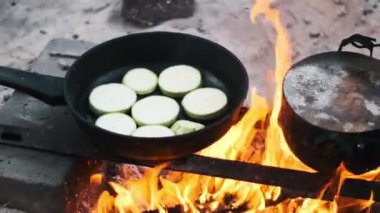 Bir tavada kabak dilimleri ve kamp ateşinde patates kızartması. Kamp yapmak ve macera yaşamak için mükemmel kırsal bir aşçılık sahnesi..