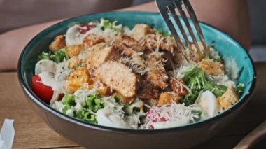 Kadın elinin yakınından taze ve lezzetli Sezar salatasını çatalla alıyor, restoranda yemeğin tadını çıkarıyor..