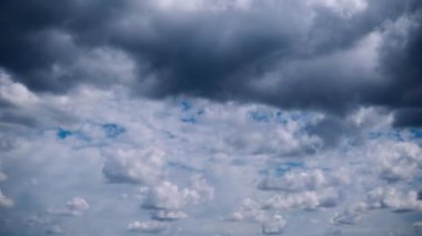 Mavi gökyüzünde hareket eden tüylü bulutların çarpıcı zamanlaması, dramatik gri fırtına bulutları yukarıda toplanıyor. Hava durumu, doğa veya değişimle ilgili projeler için ideal.