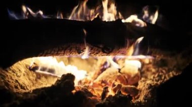 Şöminede yanan bir kütüğün yakın çekim görüntüleri karanlıkta titreşen alevler. Kışla, sıcaklıkla, evle ve ateşin yanında sıcak akşamlarla ilgili projeler için mükemmel..