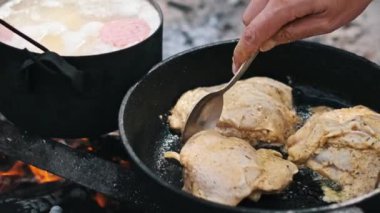 Üç parça tavuk bir kamp ateşinde tavada kızartılıyor. Doğada yemek yapmak, izci kampı, hayatta kalmak..